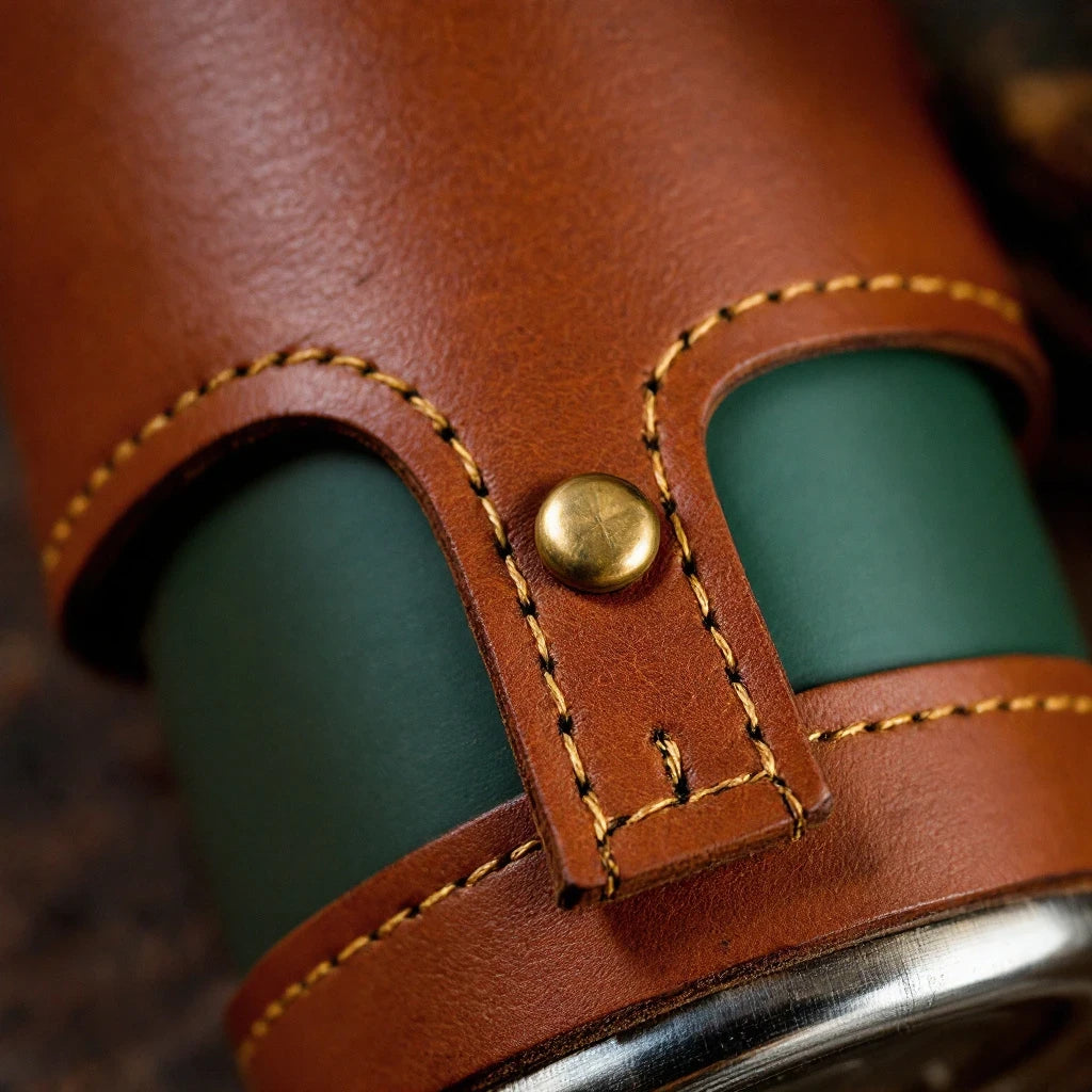 Larkwell The Journey Flask in forest green with a hand-stitched tan leather sleeve and brass rivet detail.